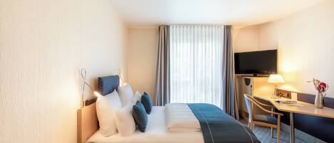 Una habitación de hotel con cama, escritorio, silla, televisor y lámpara.