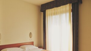 A hotel room with a bed, a bedside table, and a window with curtains. - Hotel Palazzo dei Priori (Siena)