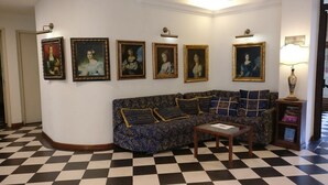 A room with a checkered floor, a patterned sofa, and a wall with framed portraits. - Hotel Palazzo dei Priori (Siena)