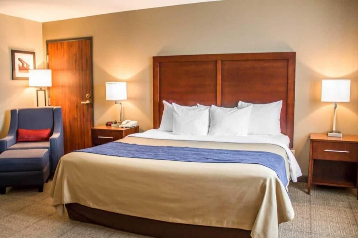 Una habitación de hotel con una cama grande, dos mesitas de noche, una silla y una puerta de madera.