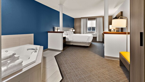 A hotel room with a large bed, a separate sitting area with a desk and chair, a bathroom with a bathtub, and a window providing a view. - Comfort Inn & Suites Fremont (Fremont)