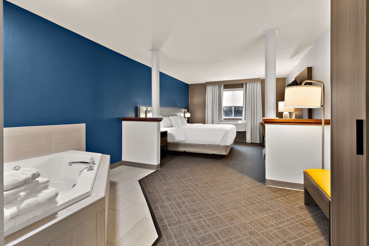 Une chambre d’hôtel dotée d’un grand lit, d’un coin salon séparé avec un bureau et une chaise, d’une salle de bain avec baignoire et d’une fenêtre offrant une vue.