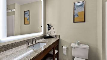 A bathroom with a granite countertop sink, a mirror, a towel rack, and a toilet.