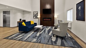 A modern living room with a blue sofa, a grey armchair, a coffee table, and a fireplace. - Comfort Inn & Suites Fremont (Fremont)