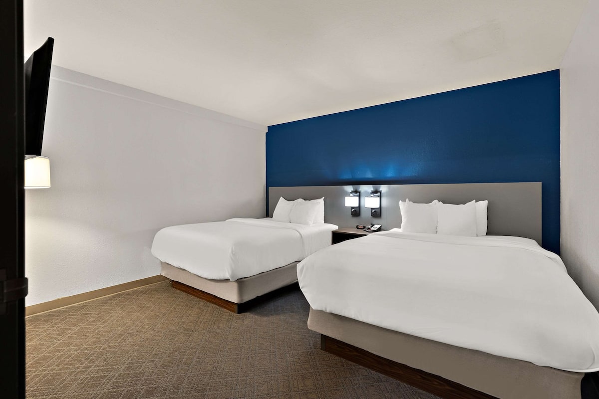 Une chambre d’hôtel avec deux lits, un grand téléviseur à écran plat et une table de chevet avec une lampe.