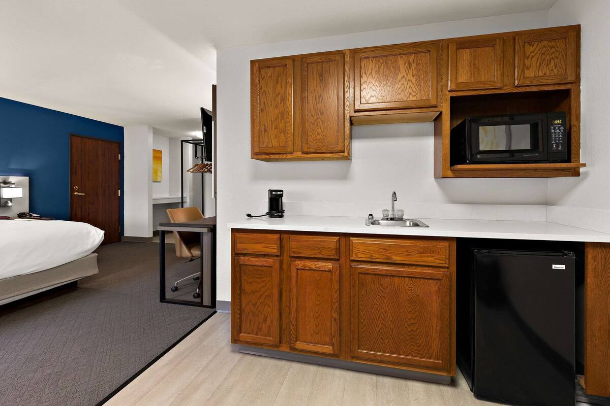 Une chambre d’hôtel compacte comprenant un coin cuisine, un lit, un bureau et une chaise.