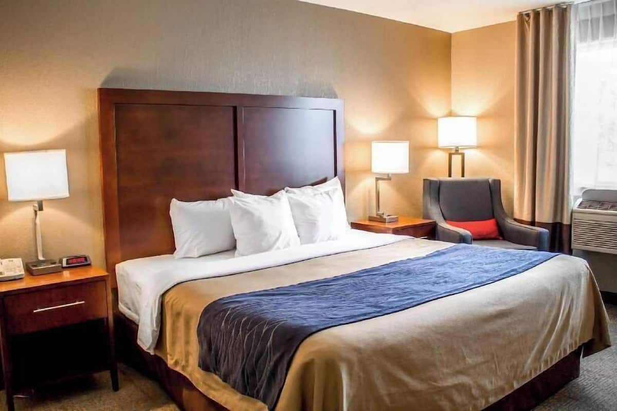 Une chambre d’hôtel avec un grand lit, deux tables de chevet avec des lampes, une chaise et une fenêtre avec des rideaux.