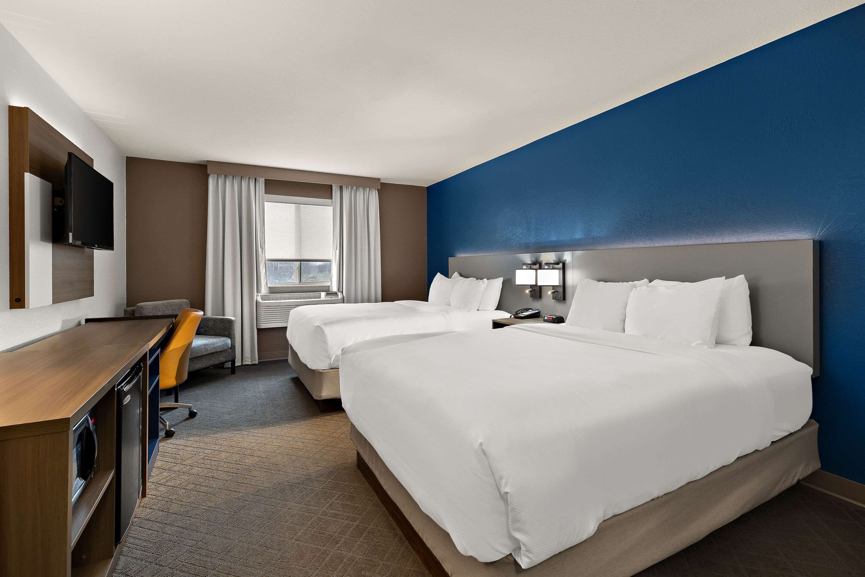 A hotel room with two beds, a desk with a television, a chair, and a window with curtains.