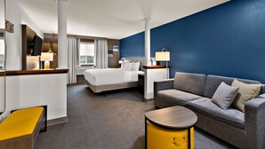 A hotel room with a bed, a sofa, a small table, and a desk with a lamp.