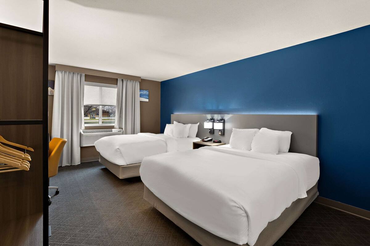 Une chambre d’hôtel avec deux lits, une grande fenêtre avec des rideaux, un bureau avec une lampe et une vue sur l’extérieur.