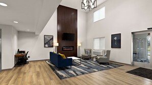 A modern hotel lobby with a wooden floor, a blue sofa, a grey armchair, and a fireplace.