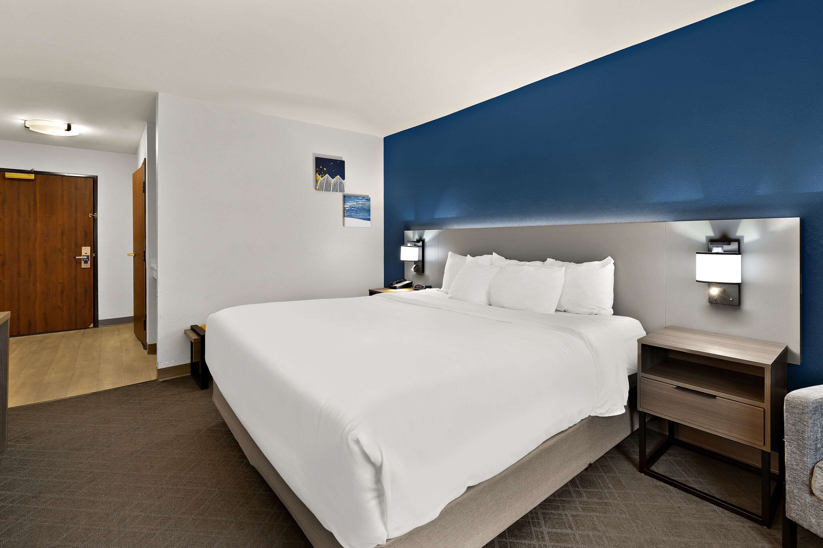 A hotel room with a large bed, a nightstand with a lamp, and a wooden door.