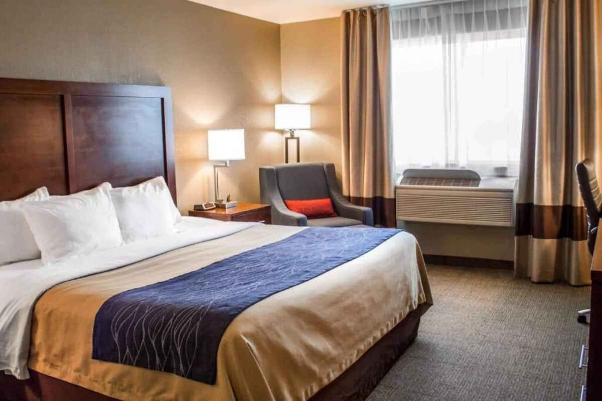 Une chambre d’hôtel avec un grand lit, un bureau avec une lampe, une chaise et un appareil de climatisation.