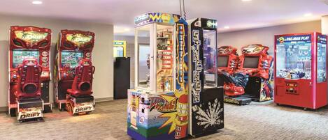 Une rangée de bornes d’arcade dans une pièce dont le sol est recouvert de moquette et qui est éclairée par des spots encastrés.
