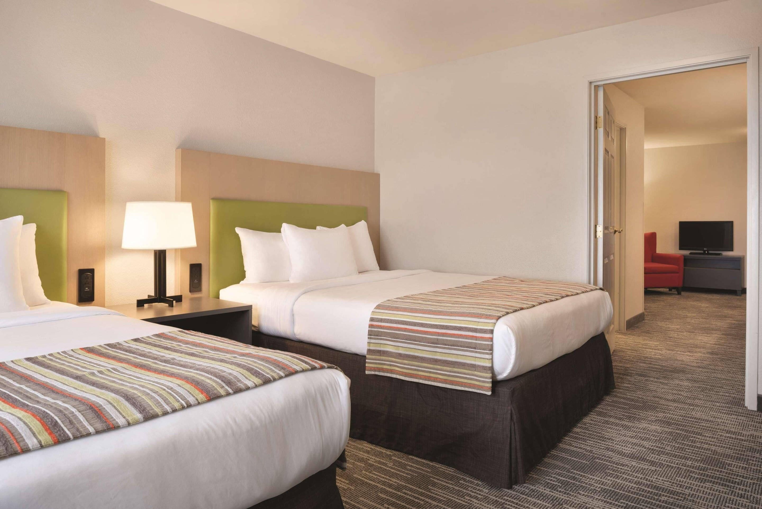 A hotel room with two beds, a nightstand with a lamp, and a television in the corner.