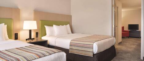 Habitación de hotel con dos camas, una mesita de noche con lámpara y un televisor en una esquina.