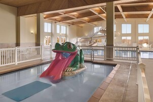 Una piscina interior con tobogán, techo de madera y barandillas blancas.