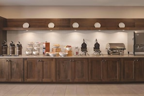 A kitchen with wooden cabinets, a countertop with various appliances and food items, and a tiled backsplash.