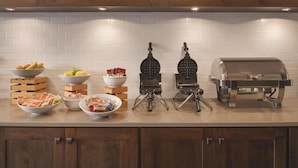 A kitchen with white tiled backsplash, wooden cabinets, and a countertop with waffle irons, a grill, and bowls of food. - Country Inn & Suites by Radisson, Galena, IL (Galena)