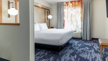 A hotel room with a large bed, a wooden headboard, a bedside table, a chair, a window with curtains, and a patterned carpet.