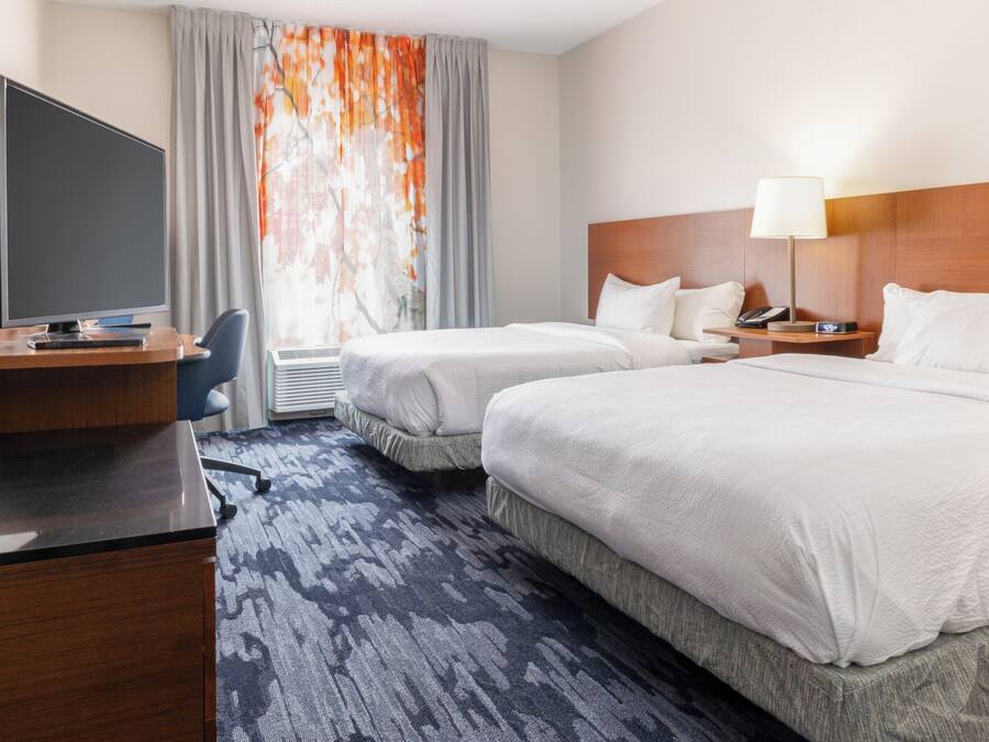 A hotel room with two beds, a desk with a computer, a chair, a lamp, and a window with curtains.
