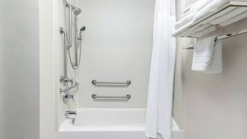 A modern bathroom with a white bathtub, grab bars, and a towel rack.