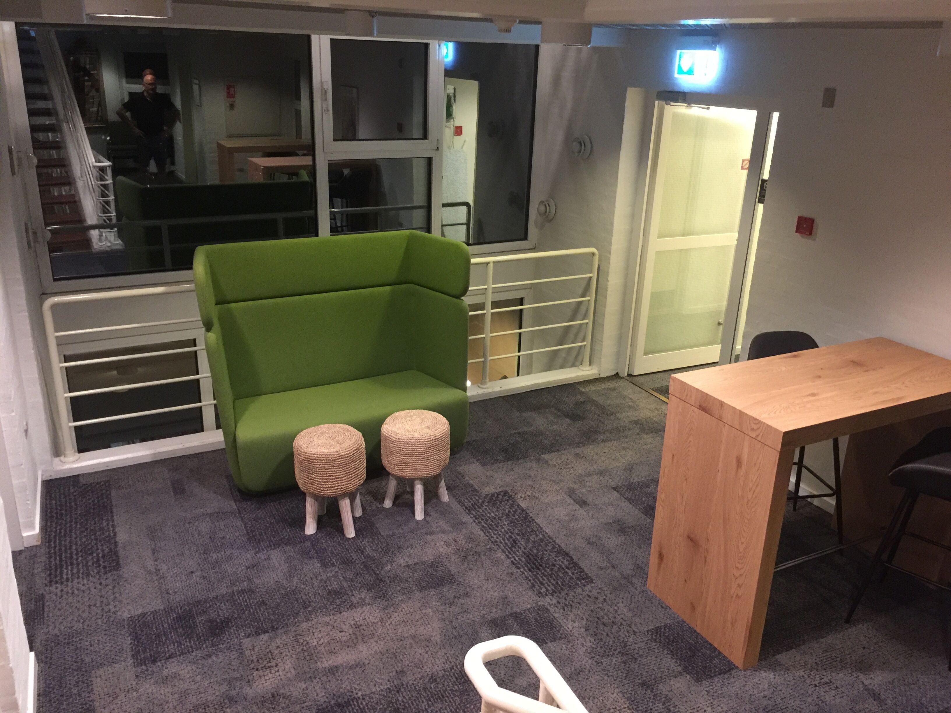 A room with a green sofa, two small stools, a wooden table, and a staircase in the background.