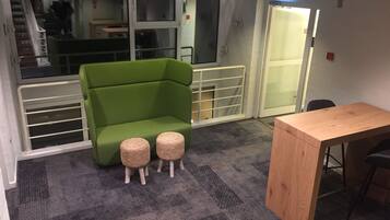 A room with a green sofa, two small stools, a wooden table, and a staircase in the background.