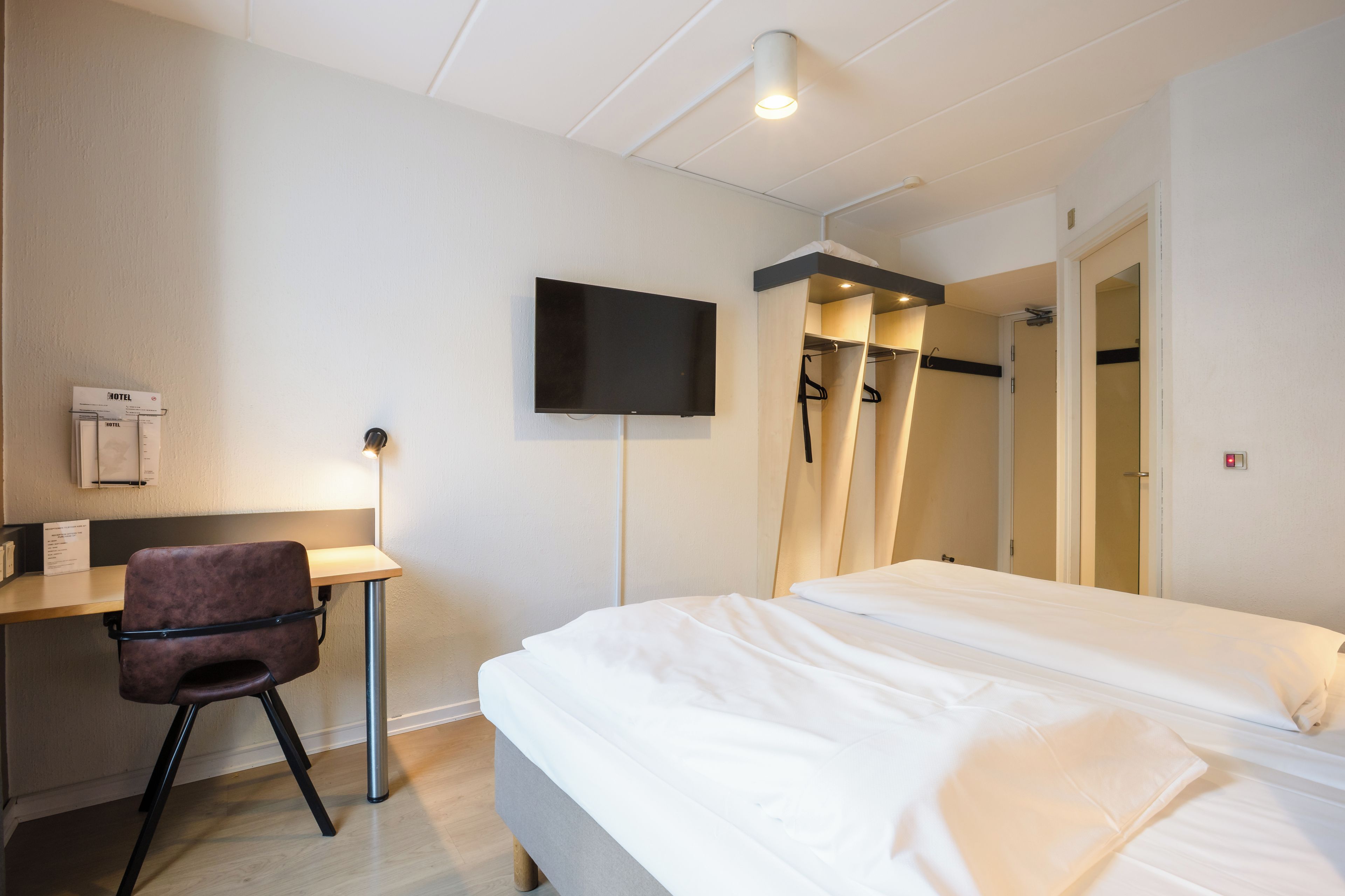 A hotel room with a bed, a desk, a chair, a television, and a shower area.