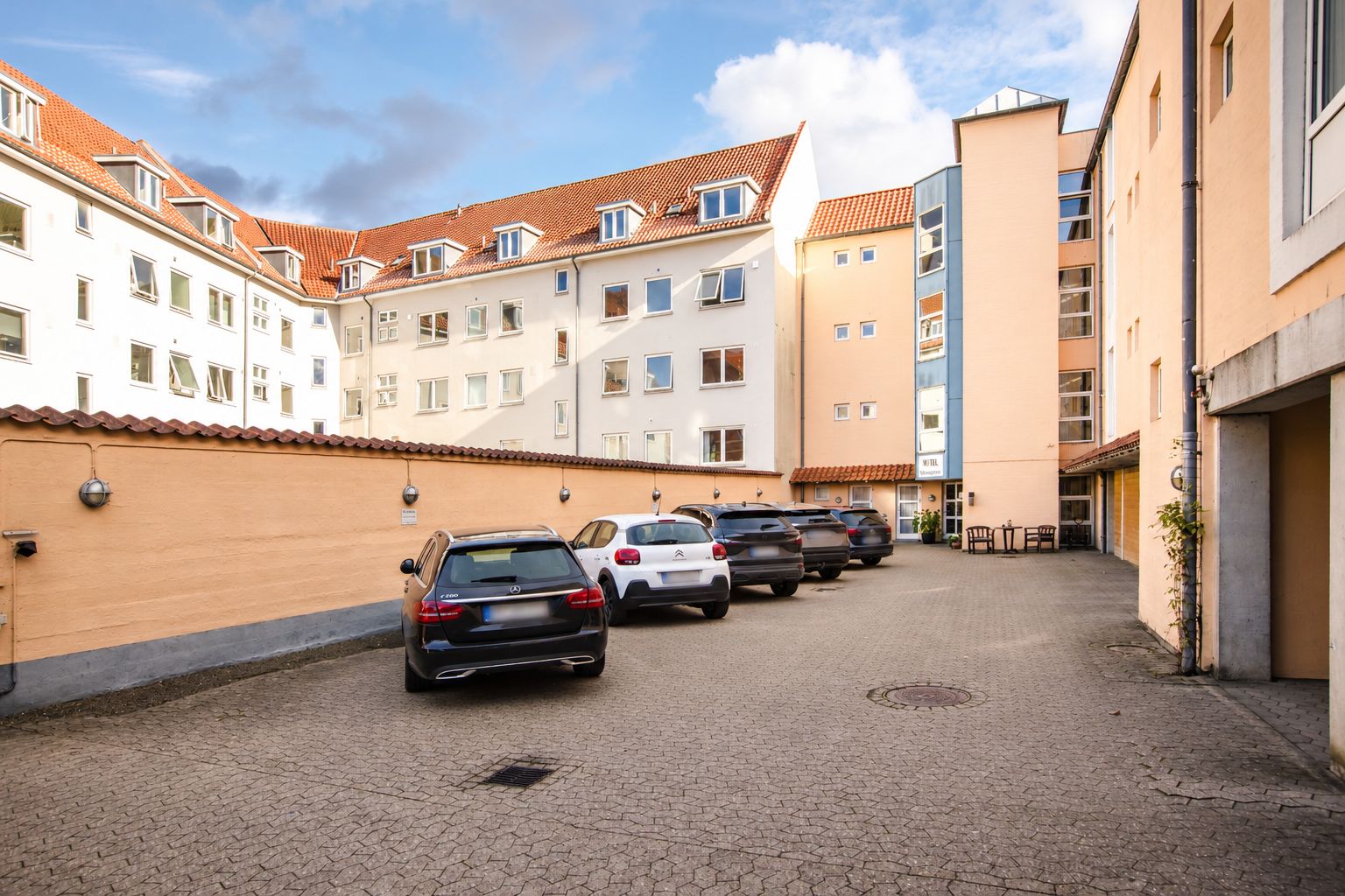 A row of parked cars in a courtyard with buildings on either side.