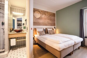 A hotel room with a bed, a bathroom with a sink and mirror, and a wall with a textured design. - City Hotel Nattergalen (Odense)