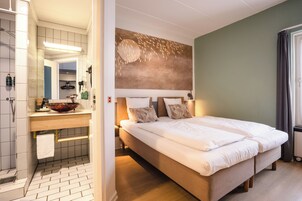 A hotel room with a bed, a bathroom with a sink and mirror, and a wall with a textured design.