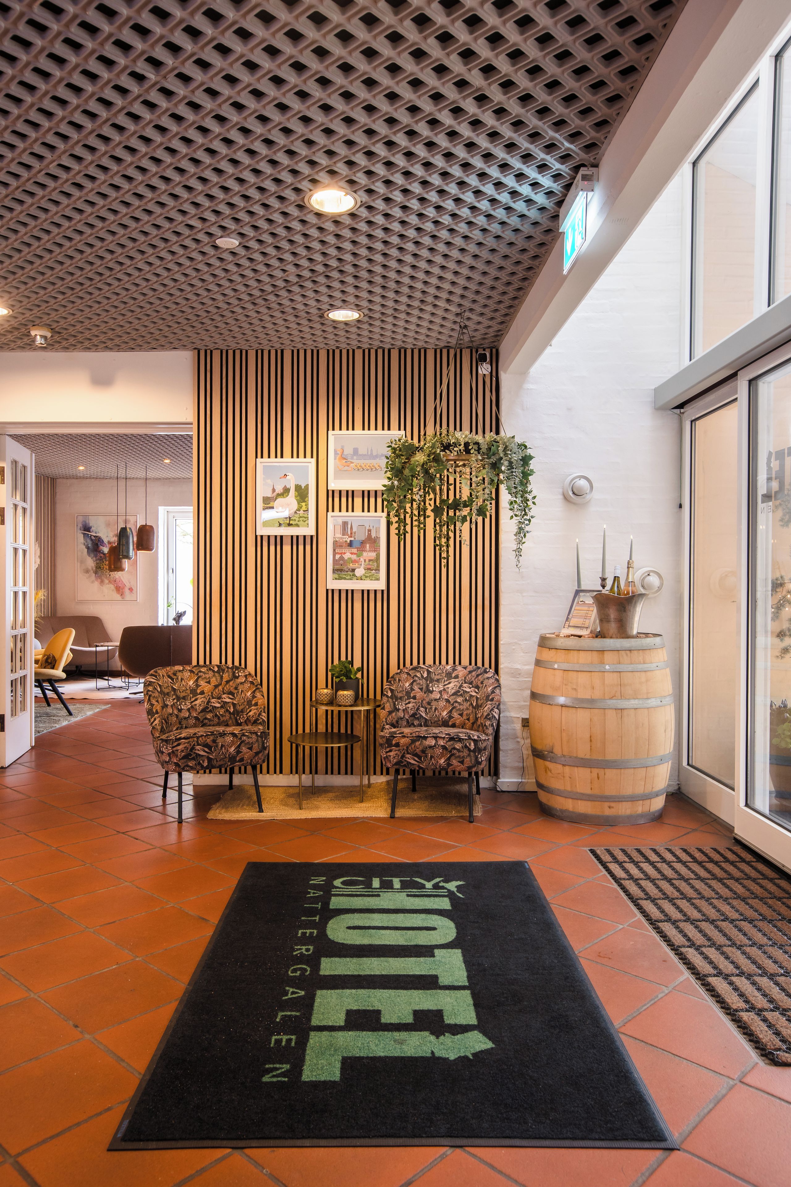 Un hall d’hôtel avec un plafond orné de motifs, des œuvres d’art encadrées, un comptoir de réception et un grand tonneau en bois.
