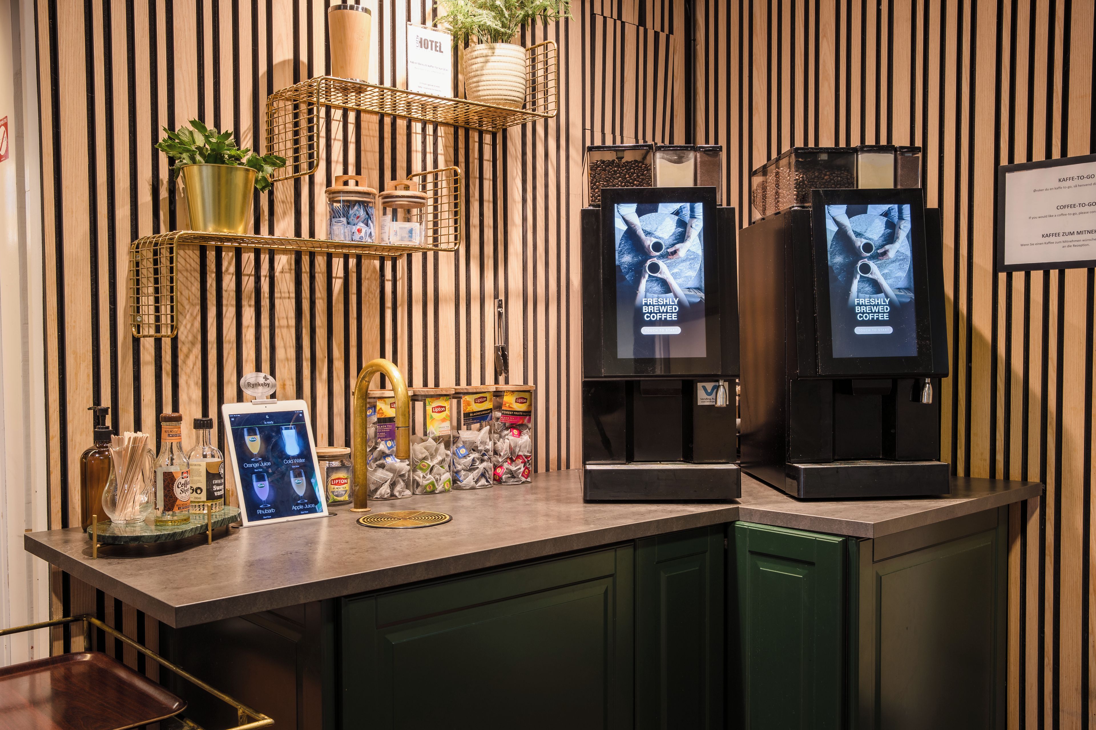 Una estación de café con un menú digital, dispensadores de café y una variedad de cápsulas de café.