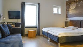 Una habitación de hotel con cama, sofá, televisión y ventana con cortinas.