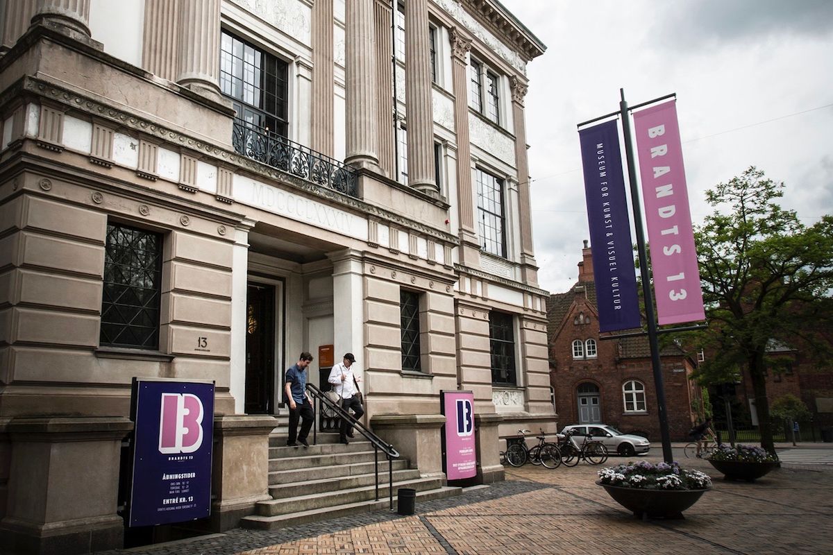 A historic building with a grand entrance, steps leading up to a door, and two banners advertising the 'Museum for Kunst & Visuel'.