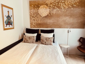 Habitación de hotel con dos camas, un cuadro de aves colgado en la pared, una mesita y una silla.