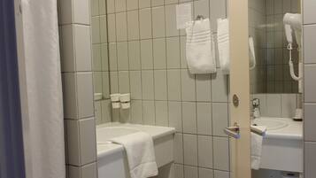 Un baño con lavamanos blanco, espejo, toallero y zona de ducha.