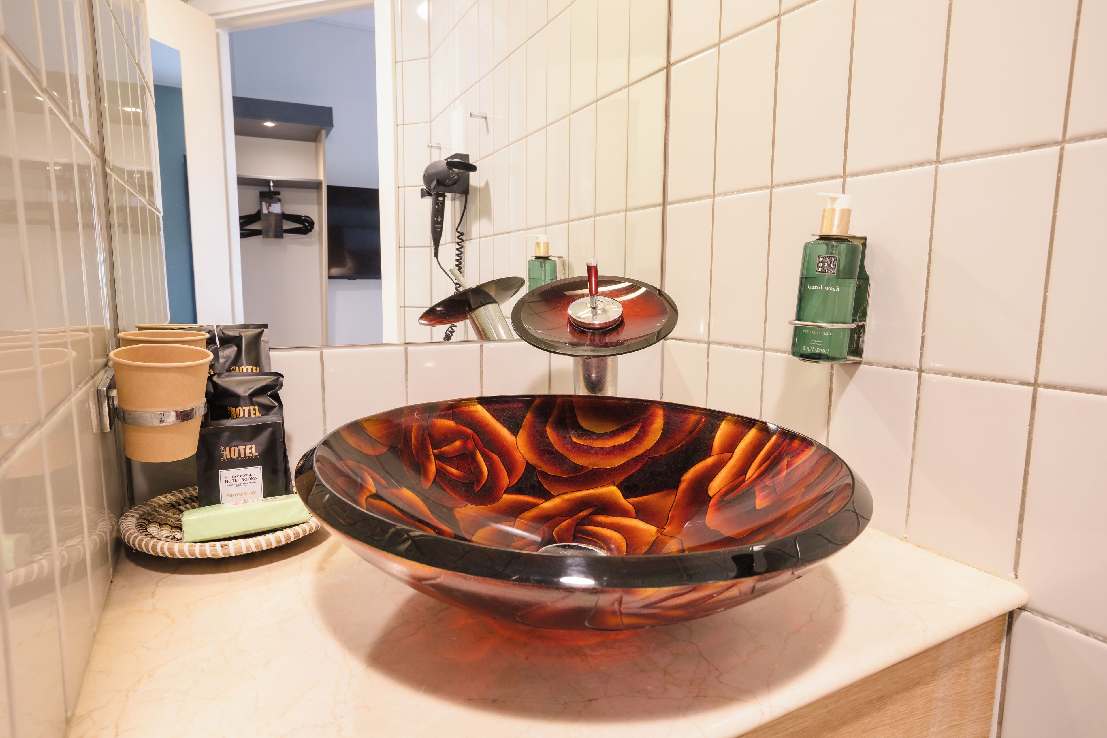 Une salle de bain avec un grand et élégant lavabo en verre, un bonnet de douche et un flacon de savon liquide pour les mains.