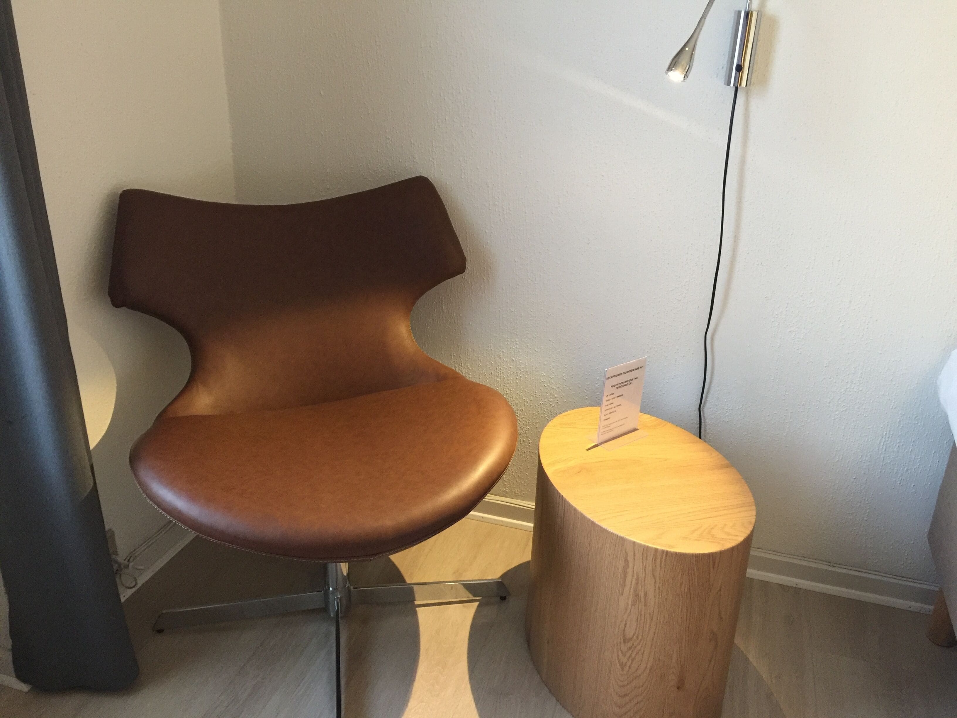 A modern chair with a unique design, a small wooden side table, and a sign on the table.