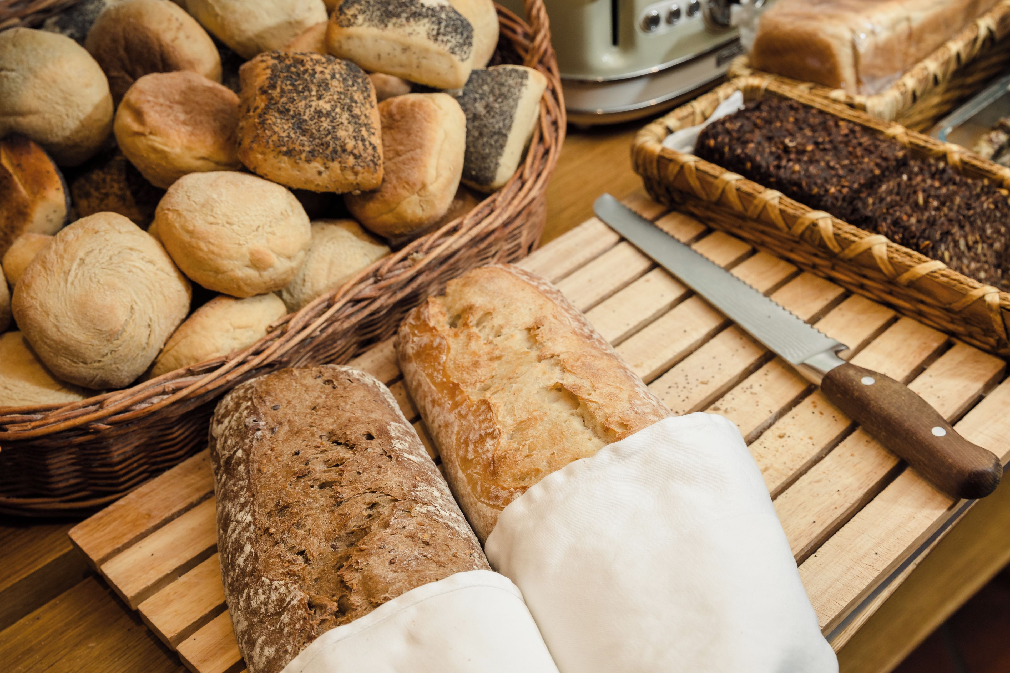 A variety of breads and a knife on a wooden cutting board.