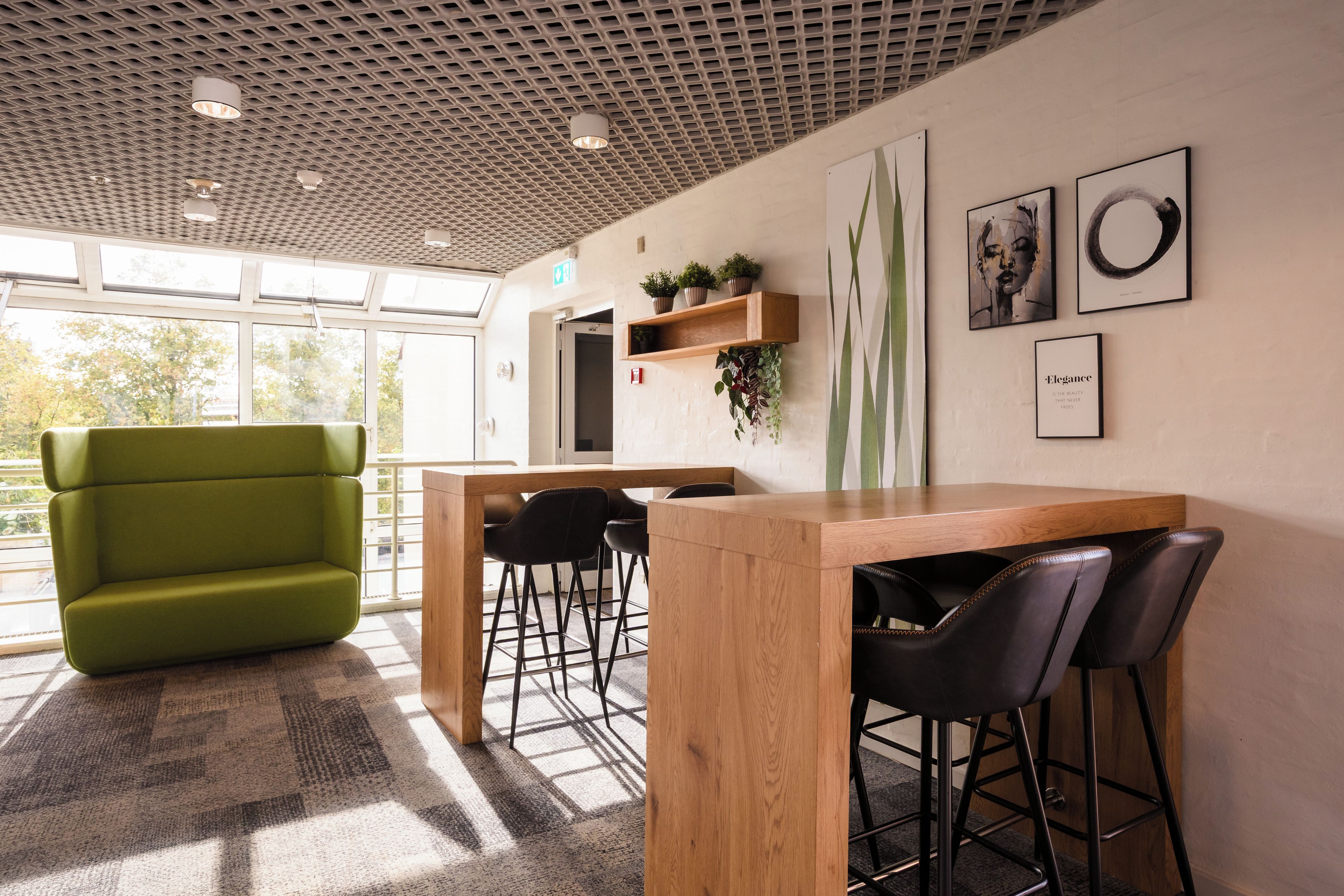 A modern office space with a green sofa, wooden desk, and bar stools.