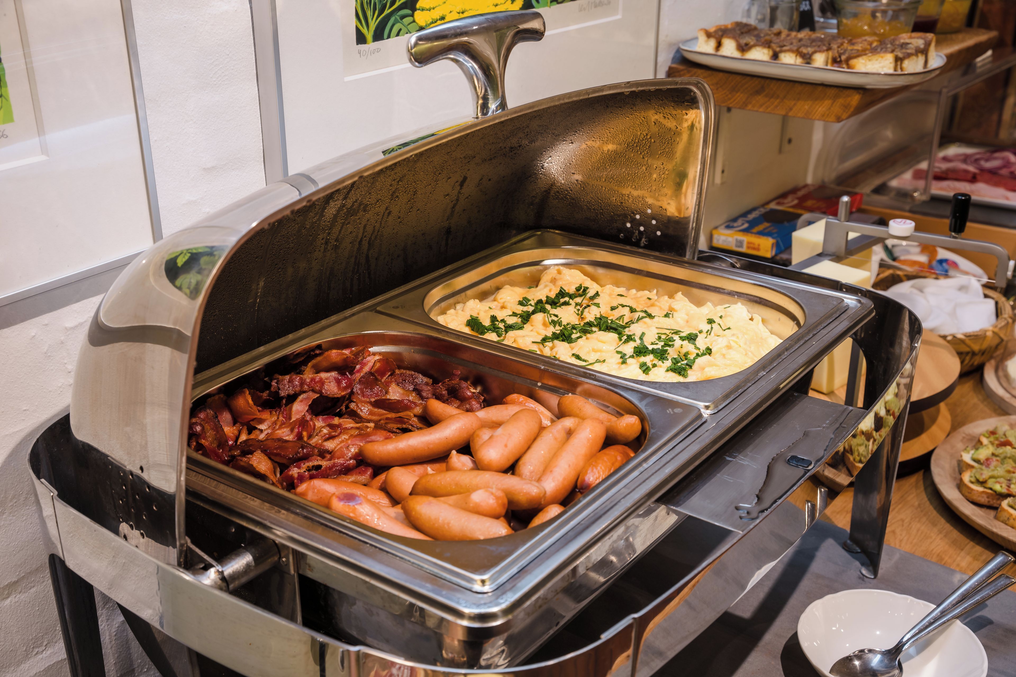 A buffet with various food options including sausages, bacon, and a dish garnished with herbs.