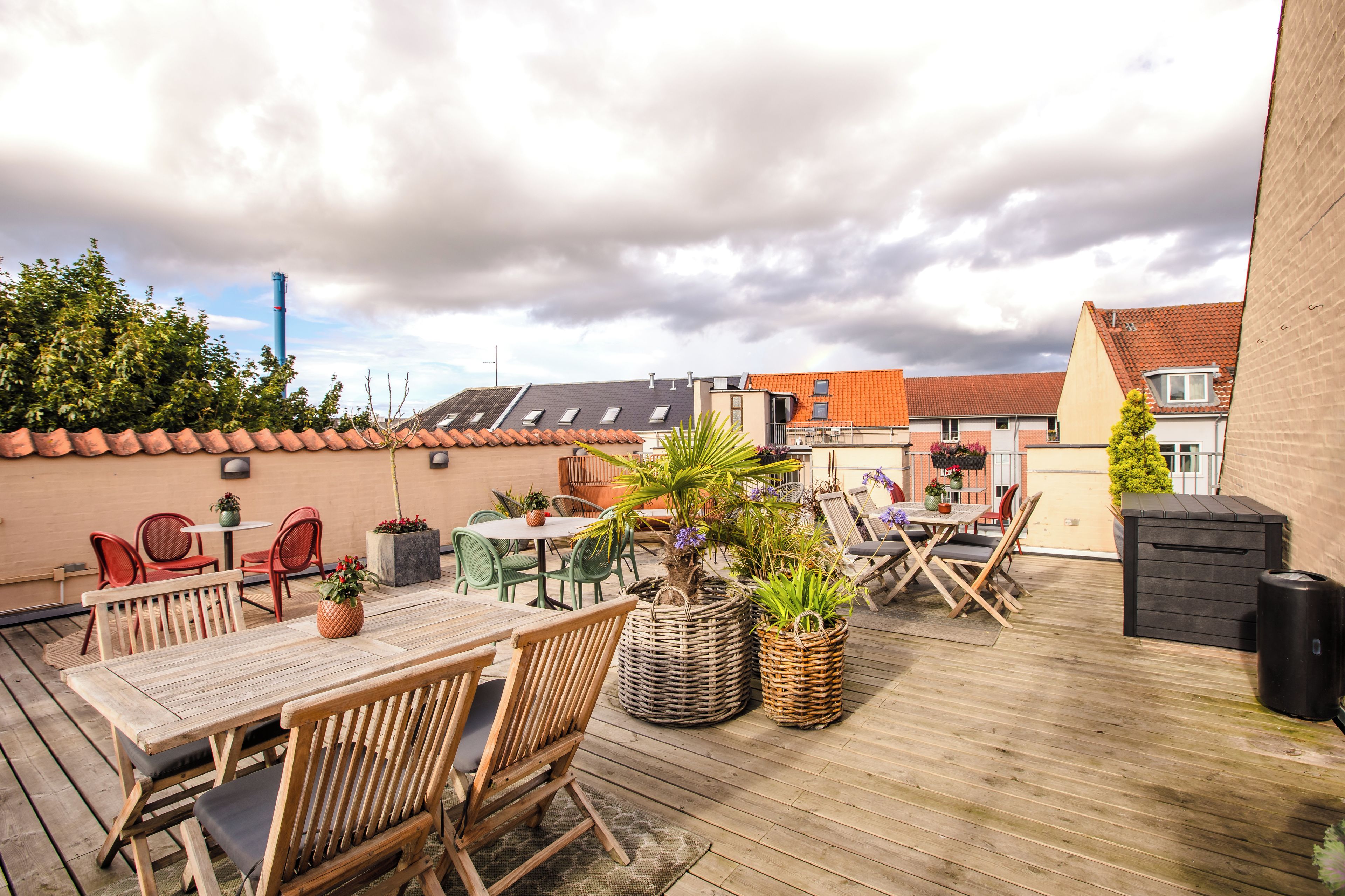 Eine Holzterrasse mit Gartenmöbeln, Blumentöpfen und Blick auf Gebäude im Hintergrund.