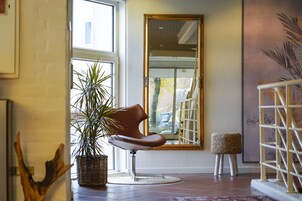 A room with a large mirror, a potted plant, a chair, and a small stool.