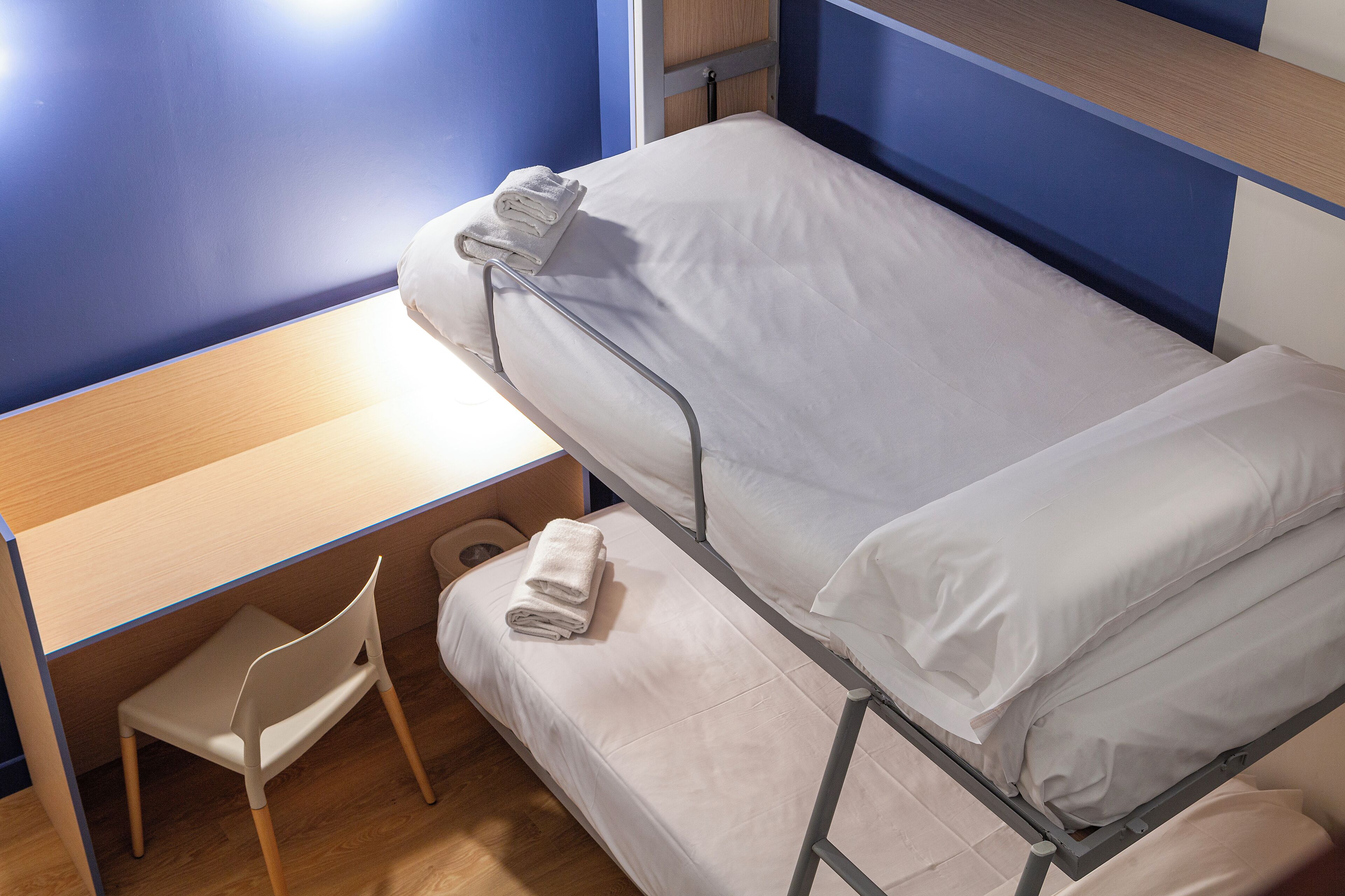 A bunk bed with white bedding, a wooden desk, and a chair in a room with blue walls.