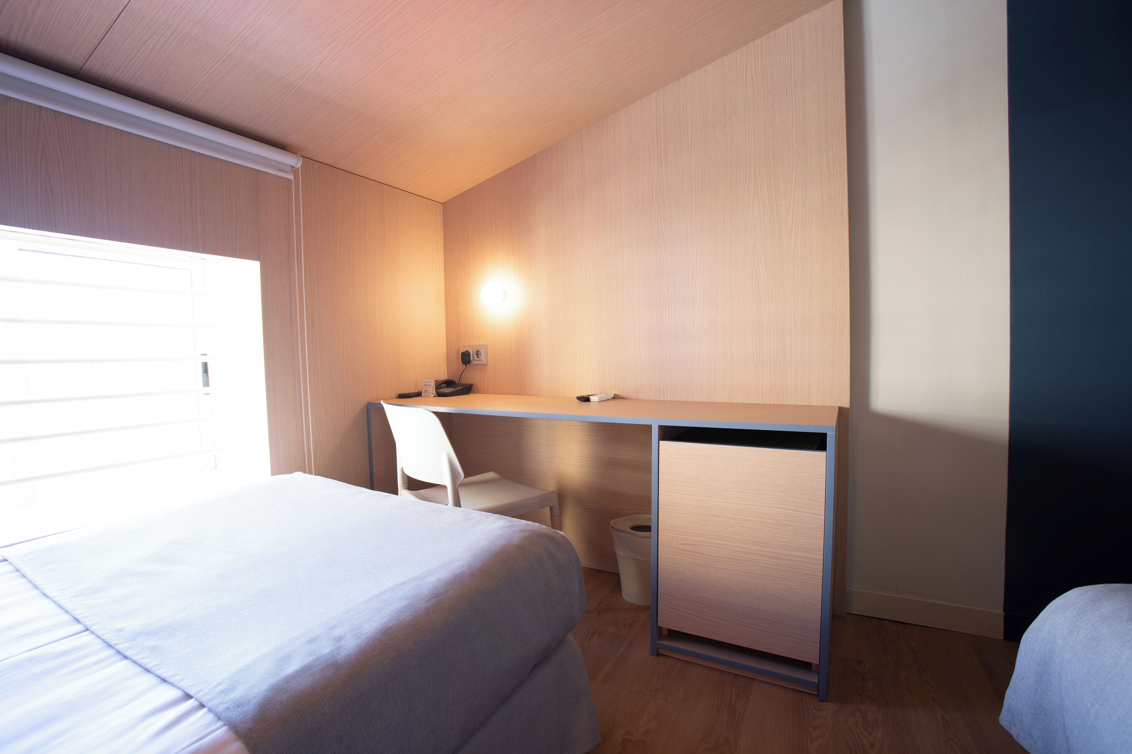 A hotel room with a bed, a desk, a chair, and a small cabinet.