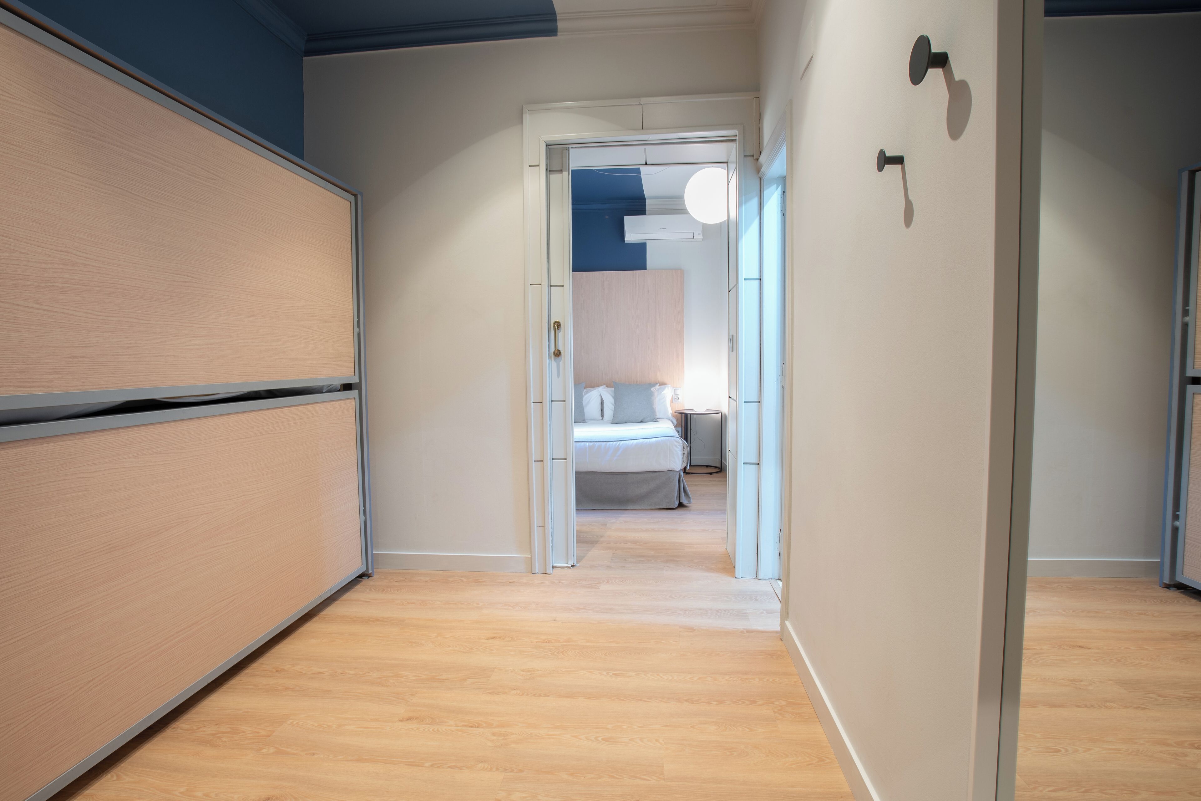 Un estrecho pasillo con suelo de madera que conduce a un dormitorio con cama y mesita de noche.