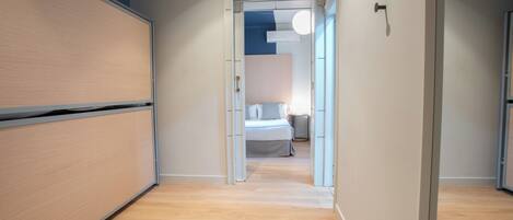 Un estrecho pasillo con suelo de madera que conduce a un dormitorio con cama y mesita de noche.