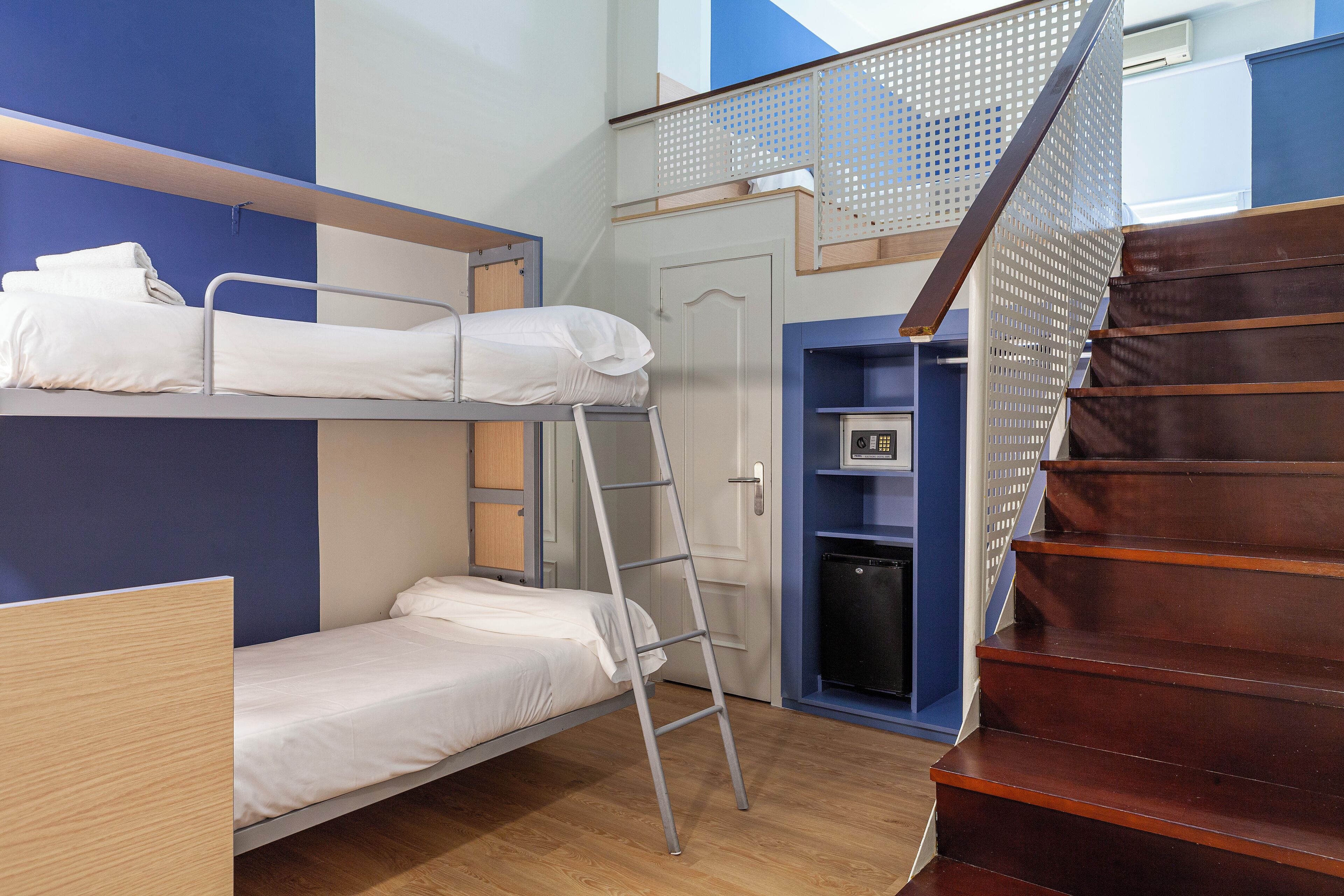 A dormitory room with bunk beds, a wooden ladder, a staircase, and a small shelf with a heater.